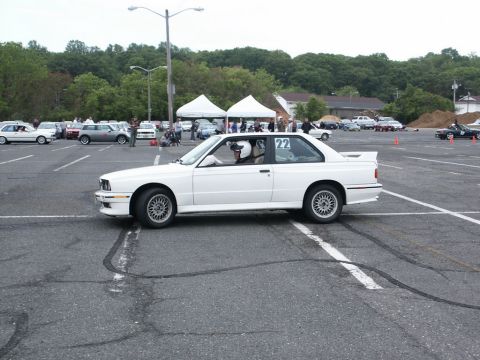 2001 Mercury Grand Marquis - A white coupe with a racing driver is parked in a lot with other vehicles and tents in the background.