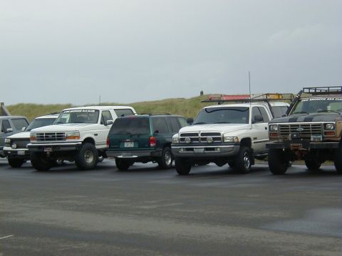 1994 Ford Explorer - A group of off-road vehicles are parked together on a cloudy day, with a grassy hill in the background.