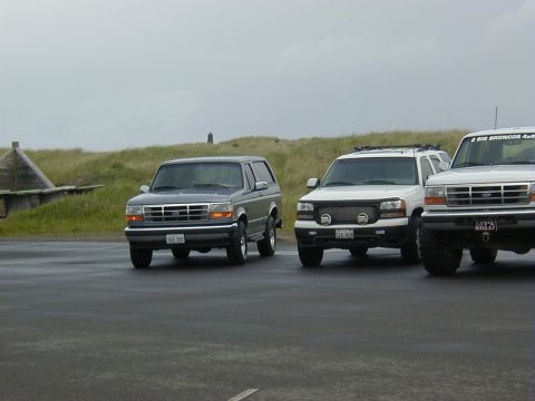 1994 Ford Explorer - Three SUVs are parked on a wet surface with grassy dunes in the background.