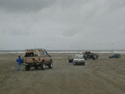 1994 Ford Explorer - Multiple vehicles are gathered on a beach with the ocean in the background under an overcast sky.