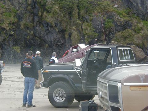 1994 Ford Explorer - Several people stand near parked pickup trucks on a beach with a rocky cliff in the background.