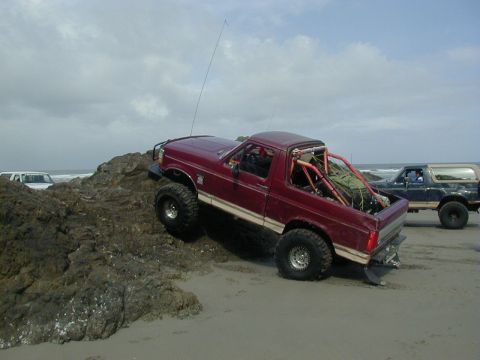 1994 Ford Explorer - A modified red pickup truck navigates a rocky beach, with another SUV visible in the background.