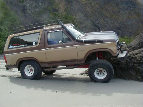 1994 Ford Explorer - Modified Ford Bronco with snorkel and roof rack driving on a beach.