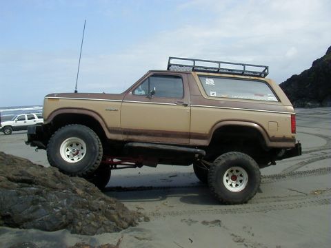 1994 Ford Explorer - A lifted two-tone Ford Bronco drives on a beach with another white SUV in the background.