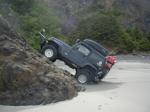 1994 Ford Explorer - Jeep Wrangler Rubicon navigating a rocky incline on a beach, equipped for off-road adventure.