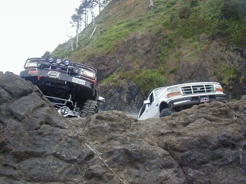 1994 Ford Explorer - Two Ford trucks navigate a challenging rocky terrain near the coast.