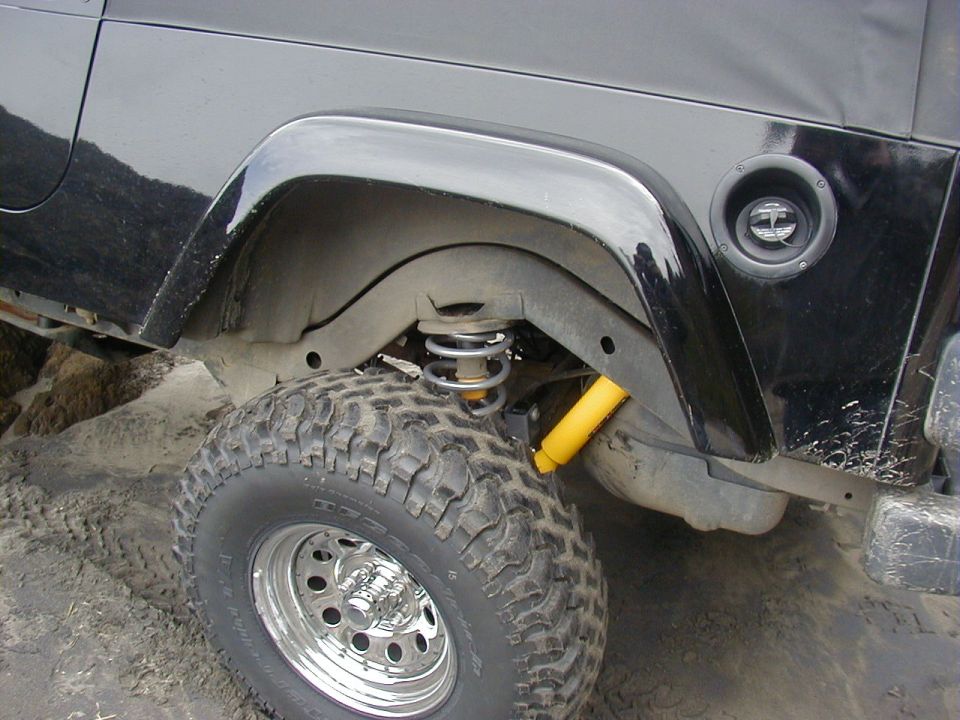 Rear wheel well of black 4x4 showing coil spring, yellow shock, mud tire on polished wheel