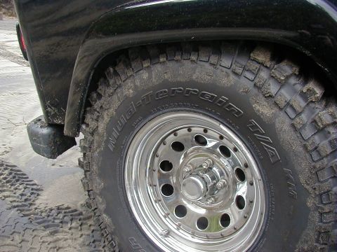 1994 Ford Explorer - Close-up of a black SUV's off-road tire and fender, covered in sand.