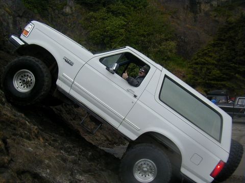 1994 Ford Explorer - A white Ford Bronco navigates a challenging rocky terrain, with another vehicle visible in the background.