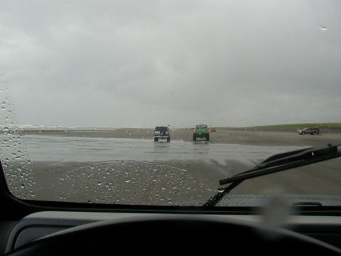 1994 Ford Explorer - Several vehicles drive on a wet beach under an overcast sky.