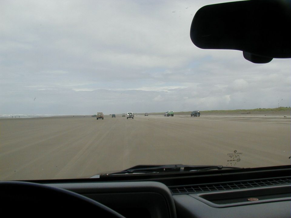 View through a windshield of trucks driving on a wide overcast beach