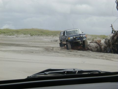 1994 Ford Explorer - A modified dark blue SUV navigates a sandy terrain near a large driftwood log.
