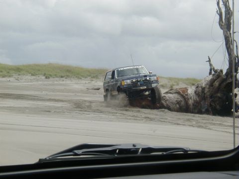 1994 Ford Explorer - SUV navigates sandy terrain next to a massive piece of driftwood on a cloudy day.