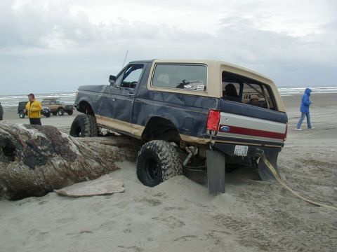 1994 Ford Explorer - A lifted Ford Bronco is stuck in the sand on a beach, with another vehicle visible in the distance.