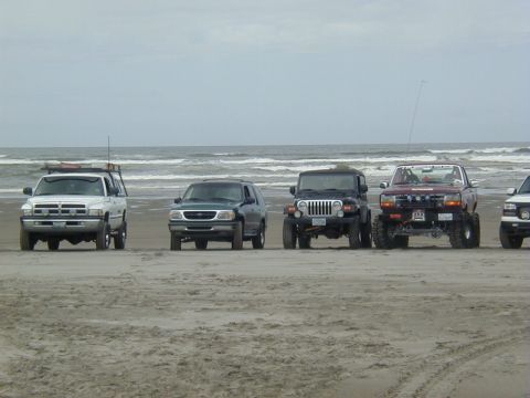 1994 Ford Explorer - A dark green SUV is parked on a sandy beach with the ocean in the background, alongside other vehicles.