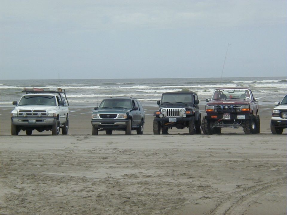 Five 4x4s including a Ram, Explorer, Jeep TJ and maroon Ford lined up on a beach