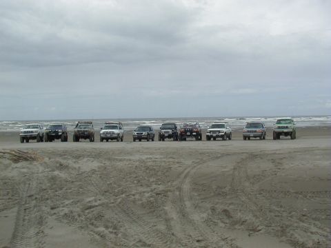 1994 Ford Explorer - A group of SUVs are lined up on the beach under a cloudy sky.