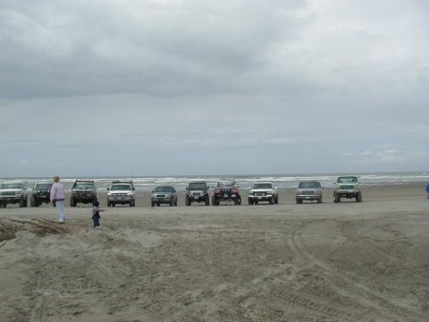 1994 Ford Explorer - Several SUVs and trucks are parked in a line on a sandy beach with the ocean in the background.