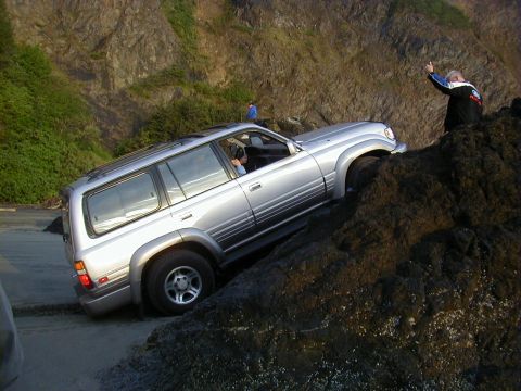 1994 Ford Explorer - A silver 1998 Toyota Land Cruiser FJ80 is shown navigating a challenging rocky incline near the coast.