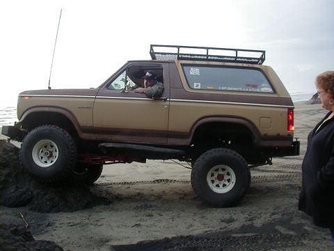 1994 Ford Explorer - Ford Bronco navigates sandy terrain near the ocean, driver at the wheel.