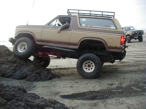 1994 Ford Explorer - This lifted Ford Bronco is navigating rocky terrain on a beach, with another vehicle visible in the distance.