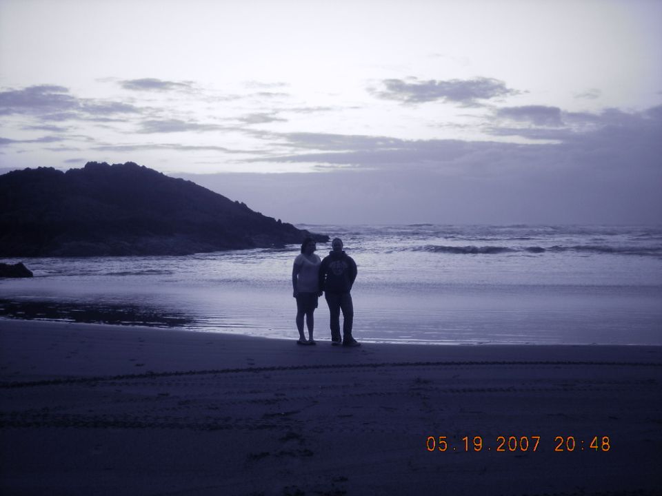Two people on a dusk beach with off-road tire tracks in the sand