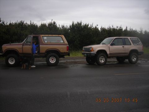 1994 Ford Explorer - Two modified SUVs are parked on the side of the road under an overcast sky.