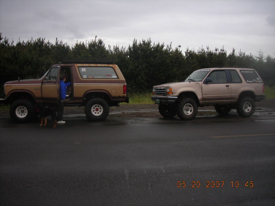 Brown Ford Bronco and tan Ford Explorer, both lifted, parked on wet pavement