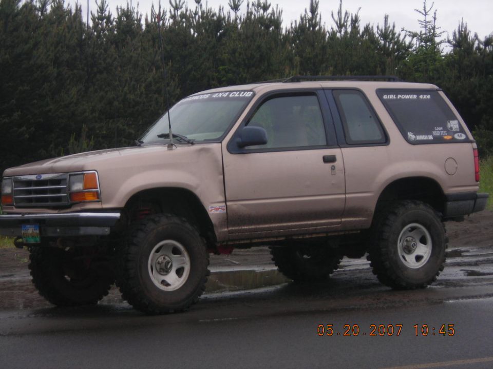 Tan 1994 Ford Explorer 2-door SUV with lifted suspension and off-road tires, viewed from the front-left