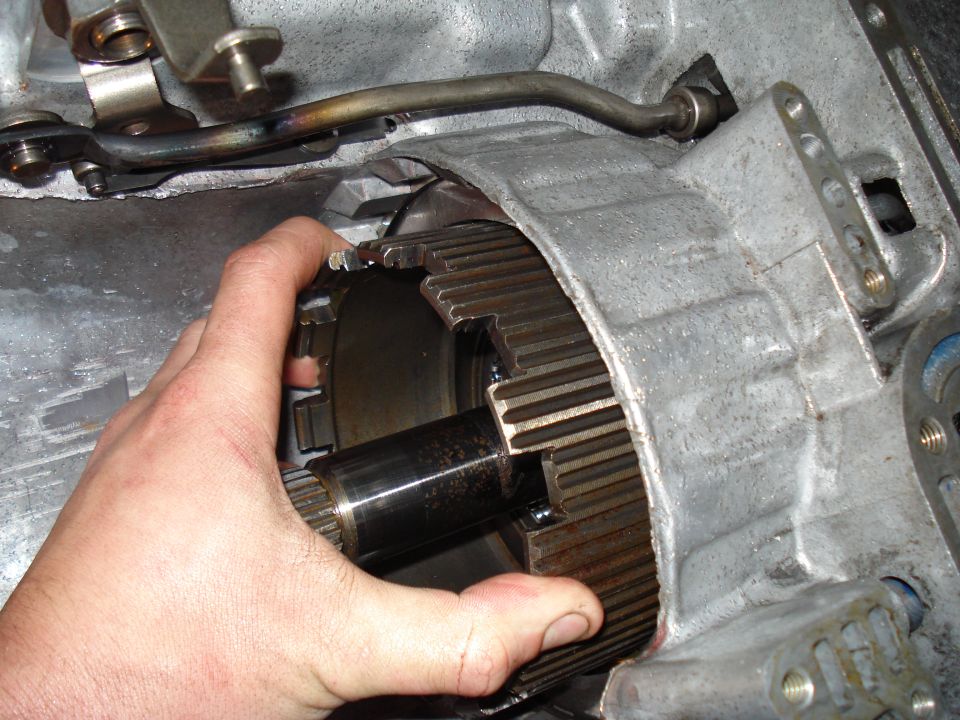 Hand holding a splined metal part inside a larger metal housing, likely a transmission