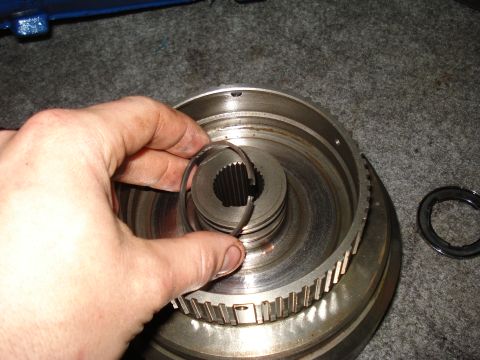 1984 Ford Bronco - A hand holds a snap ring above a transmission part, with the Supermotors.net logo in the lower right corner.