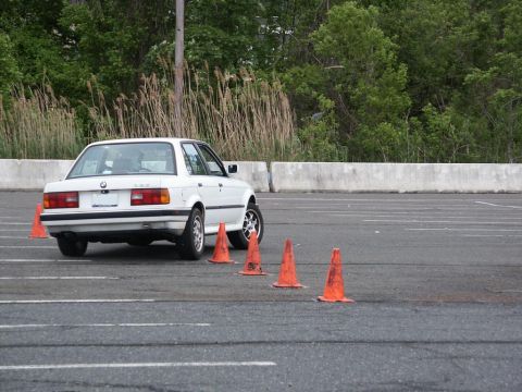 2001 Mercury Grand Marquis - A white BMW E30 sedan is seen maneuvering through orange cones on a paved surface, likely during an autocross event.
