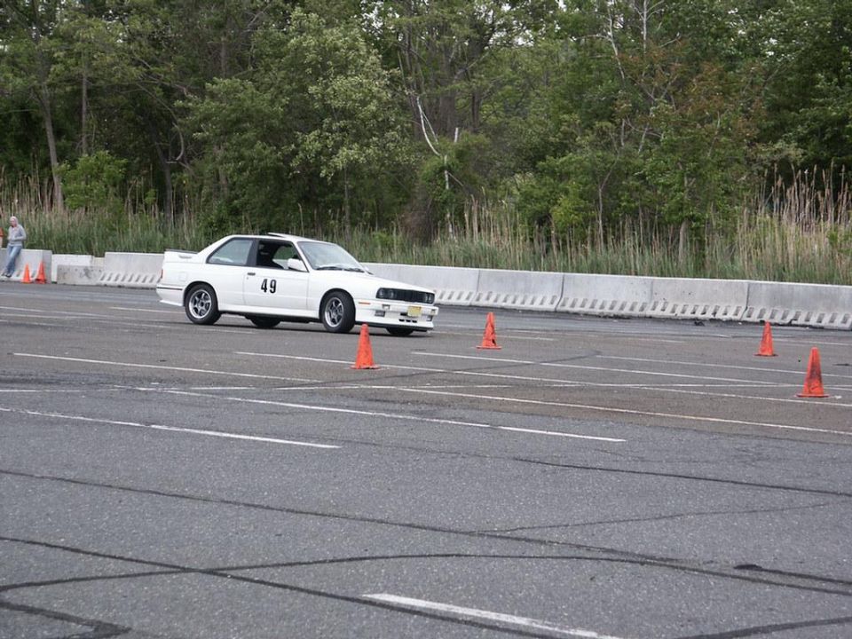 White coupe with number 49 on the door driving on a track with orange cones