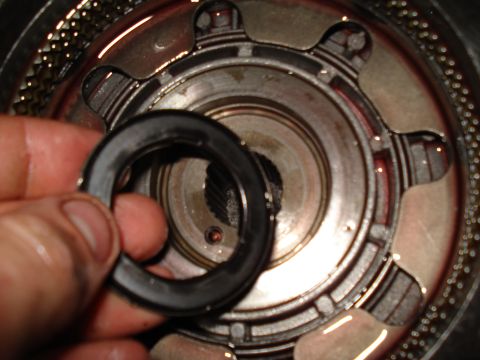 1984 Ford Bronco - A hand holds a seal over a complex metal component, likely part of a vehicle's transmission system.