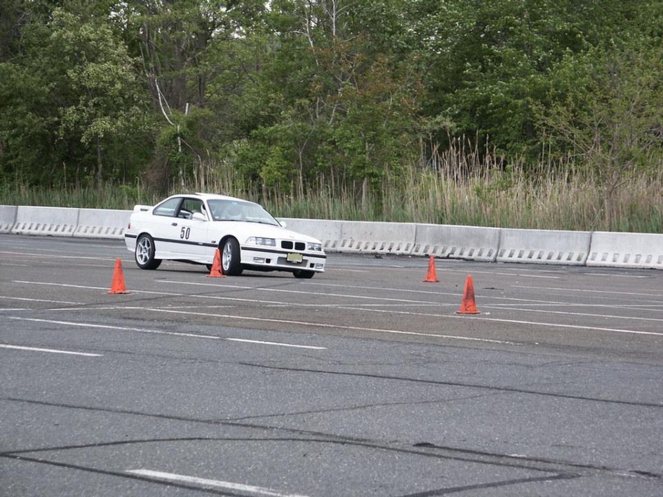 White coupe with number 50 on the door, driving on a track with orange cones