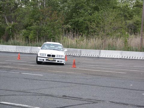 2001 Mercury Grand Marquis - White BMW E36 sedan driving on a track with concrete barriers and trees in the background.