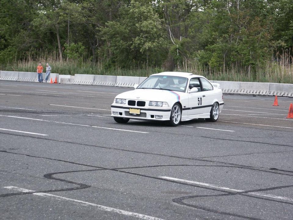 White BMW E36 coupe with racing number 50 on the side, driving on a track with orange cones