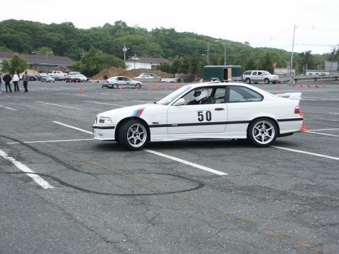 2001 Mercury Grand Marquis - A white BMW E36 coupe, number 50, participates in an autocross event on a paved course with safety cones.