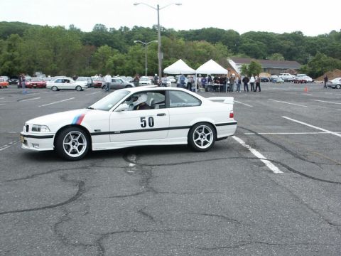 2001 Mercury Grand Marquis - White BMW M3 coupe with racing stripes and number 50 is seen at an event with other vehicles and tents in the background.