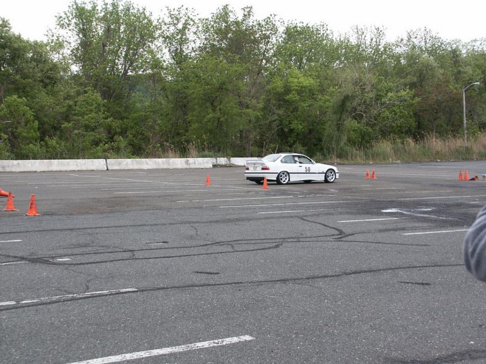 White coupe with racing number 50 on door, seen from a 3/4 front angle on a paved lot with orange cones