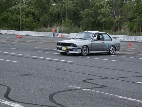 2001 Mercury Grand Marquis - A silver BMW E30 M3, identified by its distinctive body style, navigates a racetrack. The car displays the number 51 on its door and appear…