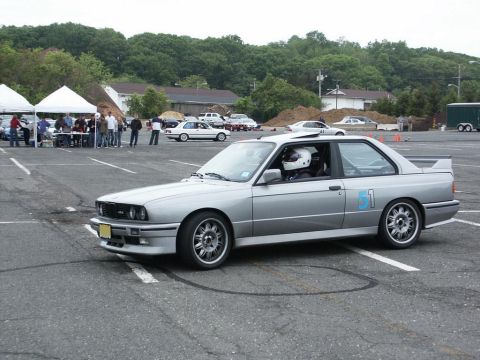 2001 Mercury Grand Marquis - Silver BMW E30 coupe with racing decals at an event, driver in helmet visible.