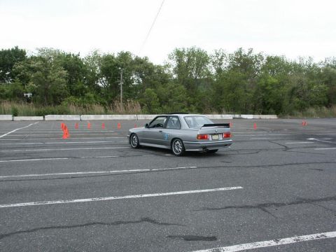 2001 Mercury Grand Marquis - A silver BMW E30 M3 navigates a course marked by orange cones on a paved lot.