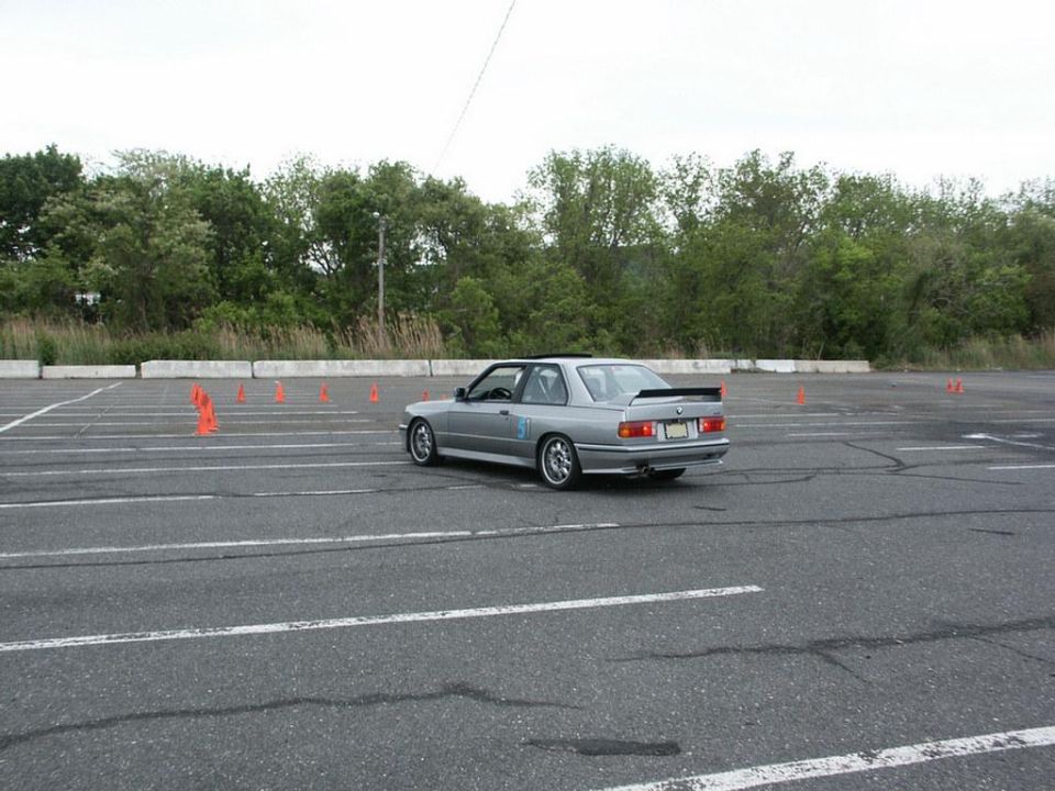 Silver BMW E30 M3 with a spoiler on a track with orange cones