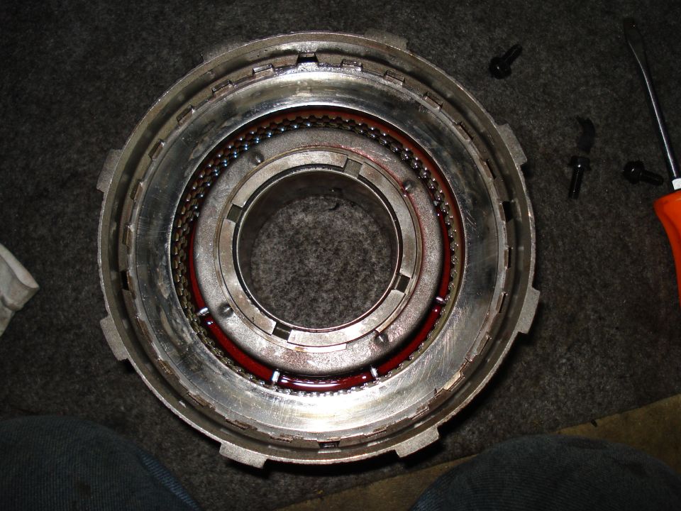 Close-up of a transmission drum with ball bearings and red fluid. A screwdriver is visible on the right