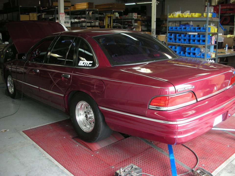 Maroon sedan with hood open on a red dynamometer platform. It has chrome trim and drag racing wheels
