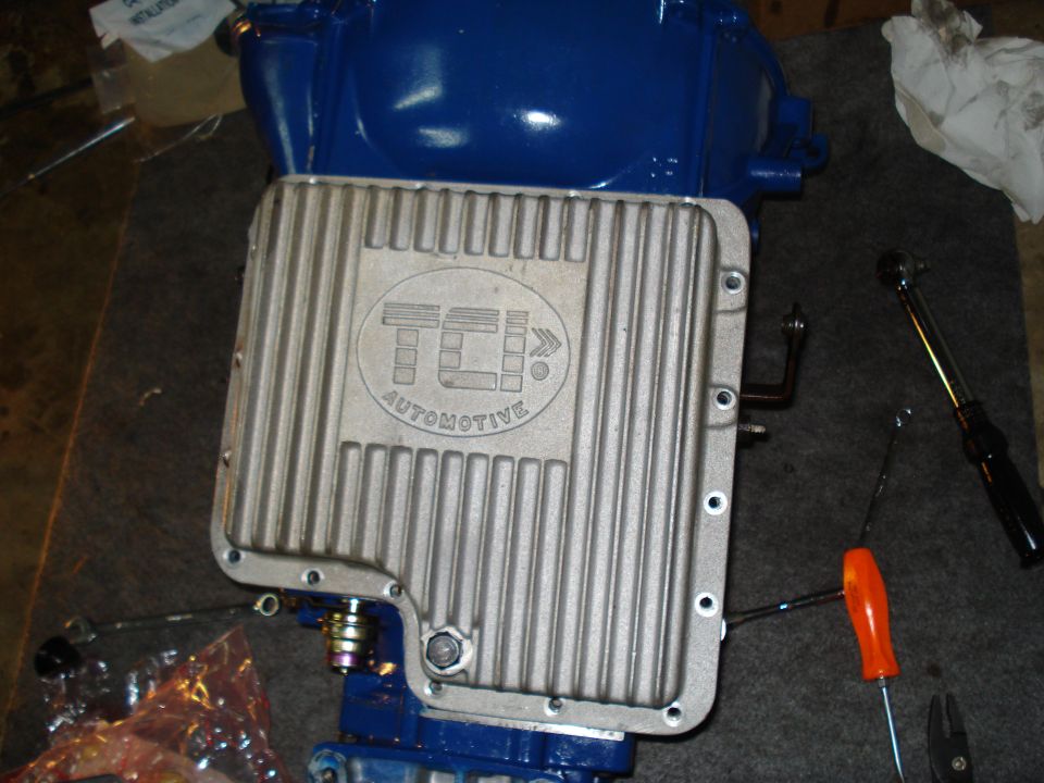 Close-up of a TCI Automotive transmission pan with a blue transmission housing underneath. Tools are on the side
