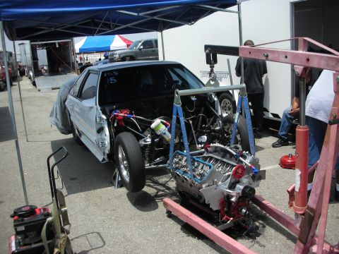 1998 Ford Crown Victoria - A drag car is shown with its engine removed and suspended by an engine hoist, indicating maintenance or modification.