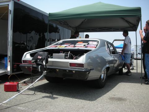 1998 Ford Crown Victoria - A silver drag car is parked with its trunk open, displaying racing stickers on the rear window and a tow rope attached.
