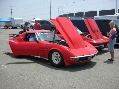 1998 Ford Crown Victoria - Two red Chevrolet Corvette Stingrays are parked with their hoods open at an outdoor event.